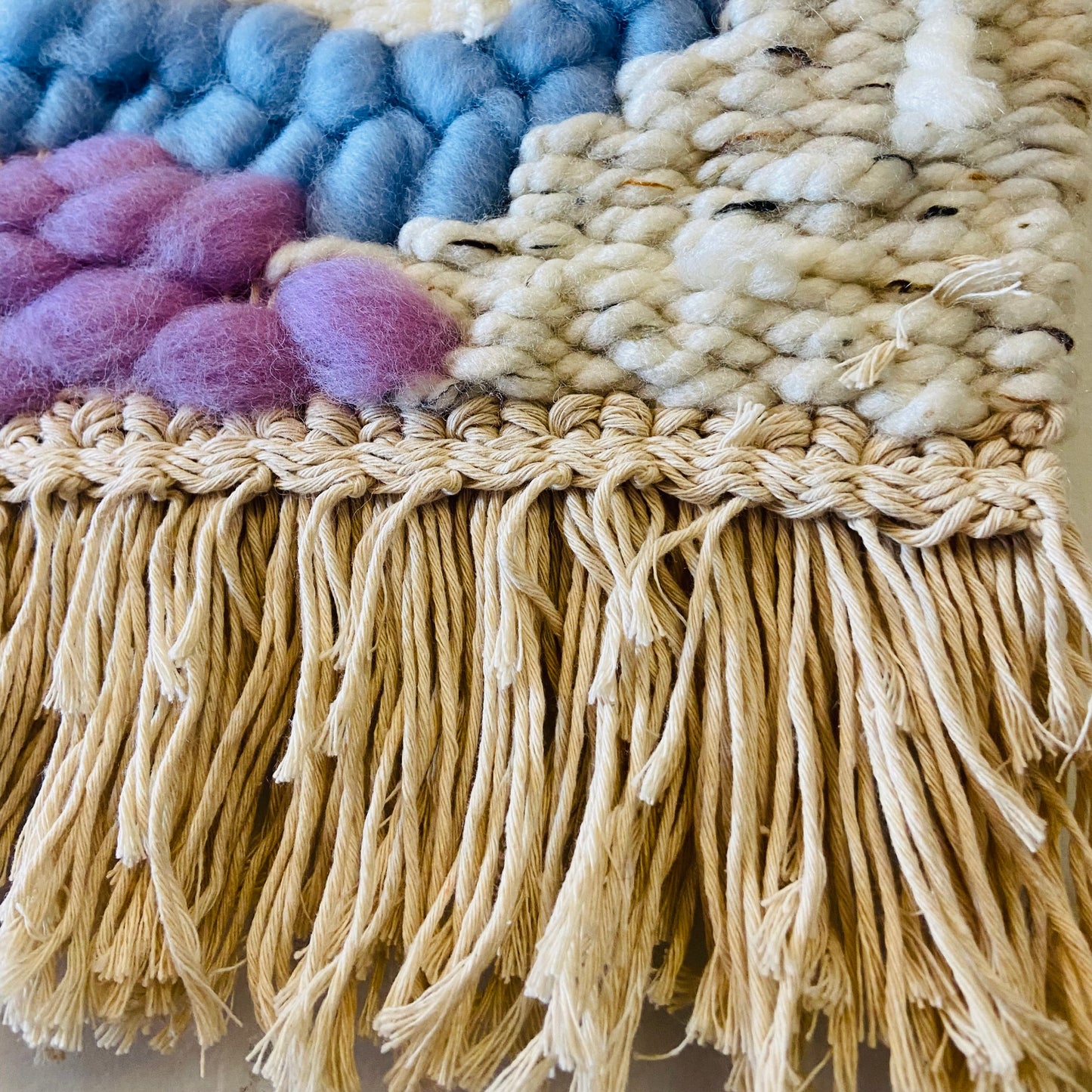 Close-up of a textured fabric with colorful pom-poms and fringes.
