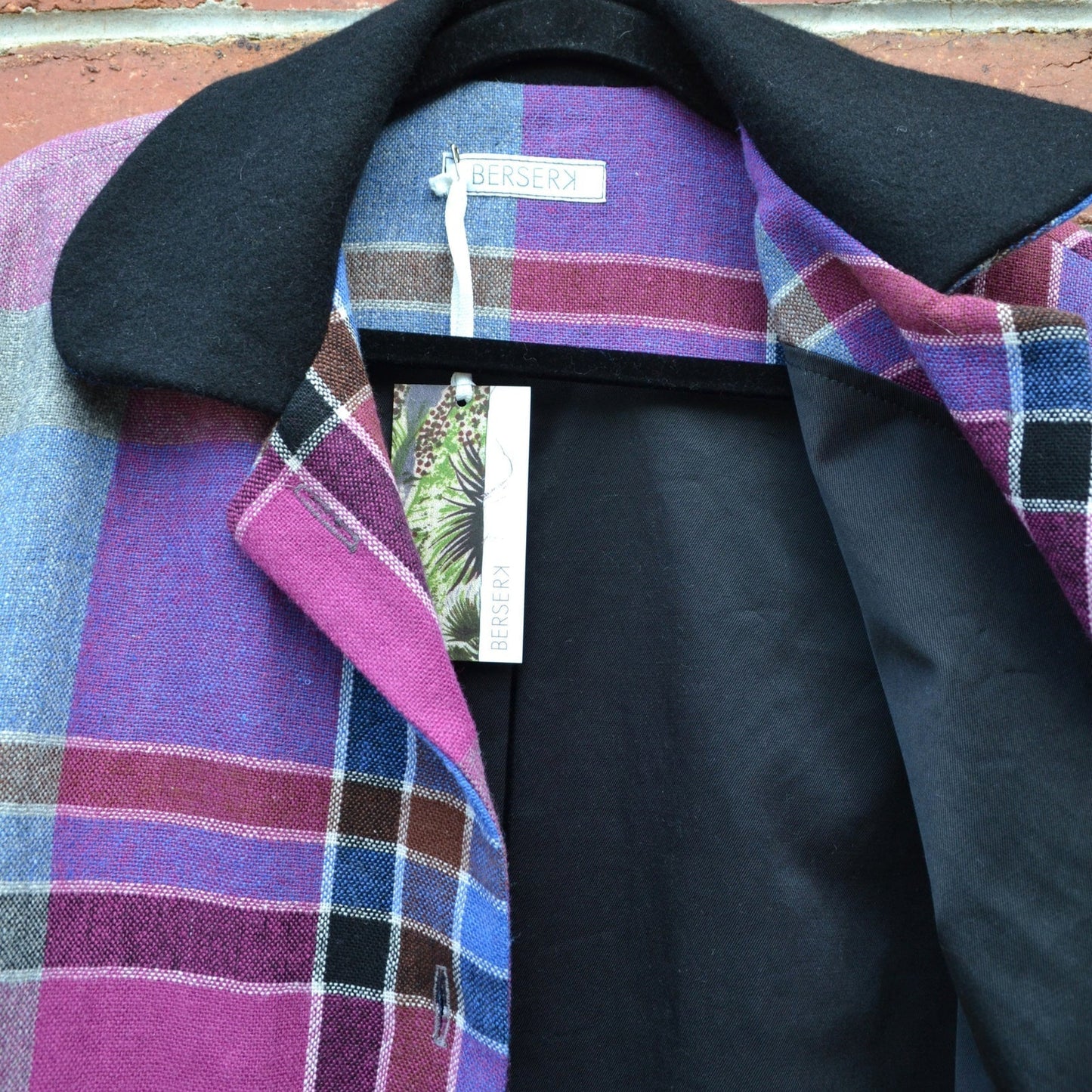 Plaid jacket with black lining against a brick wall