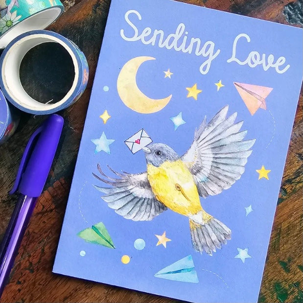 Greeting card with a bird illustration and 'Sending Love' text on a wooden surface with a pen and coffee cup.