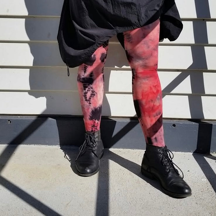 Person wearing red and black patterned leggings with black shoes standing against a wall.