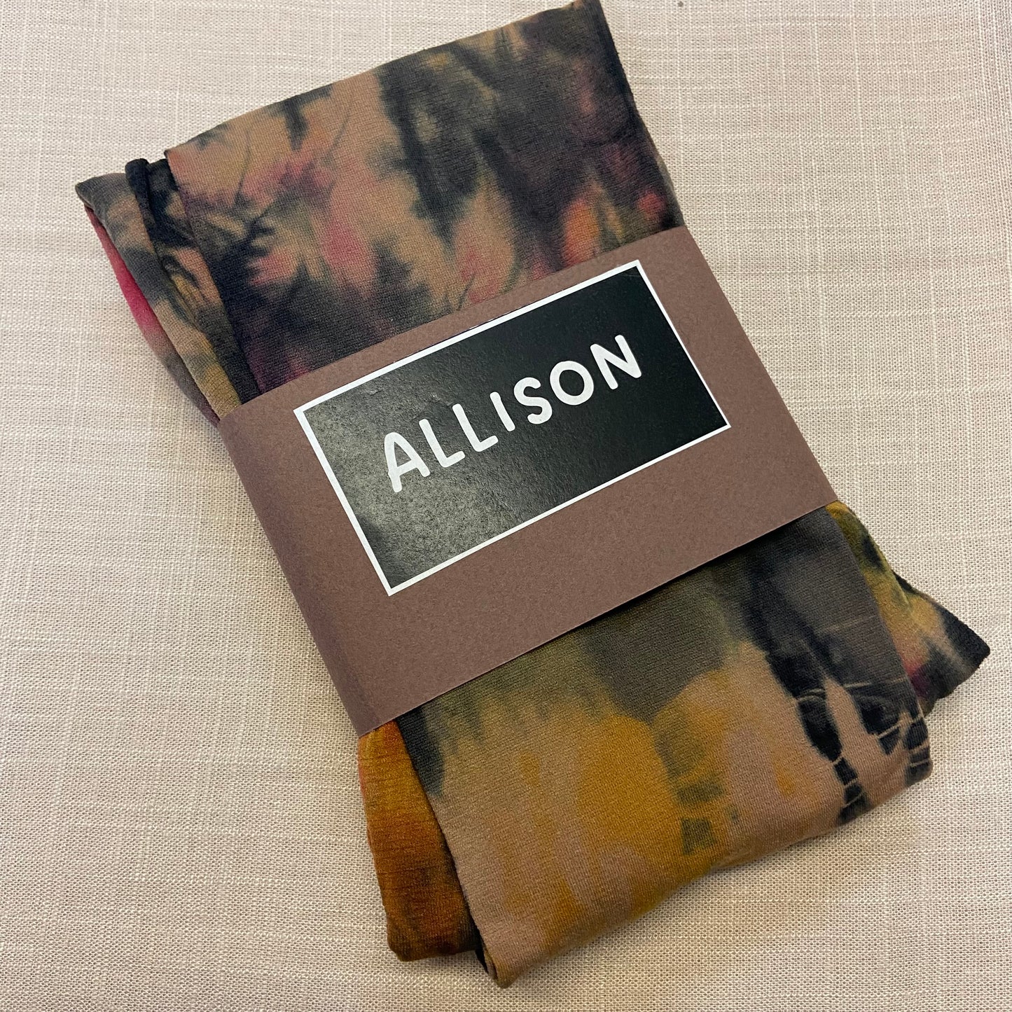 Folded tie dyed womens tights with a label reading 'ALLISON' on a beige background