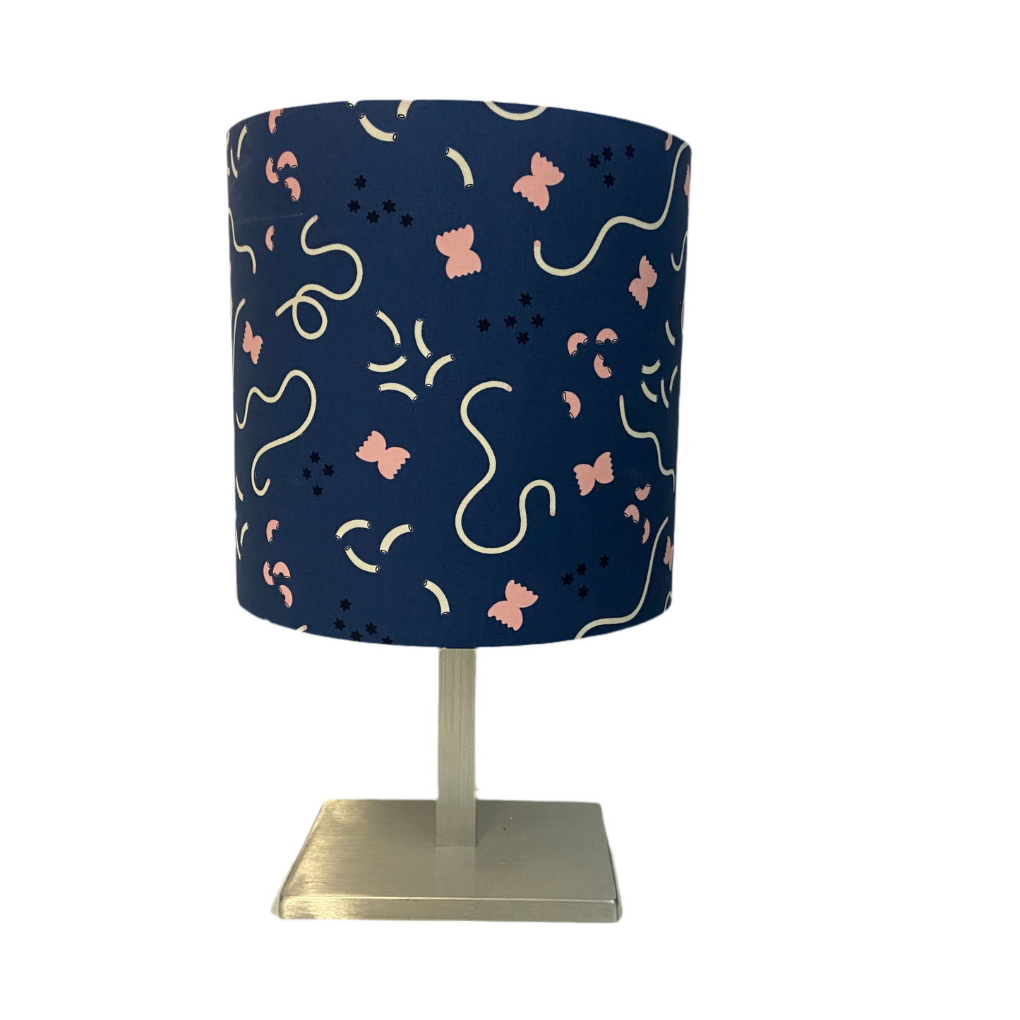 Table lamp with a navy blue shade featuring pink and white abstract pasta and macaroni patterns on a white background.