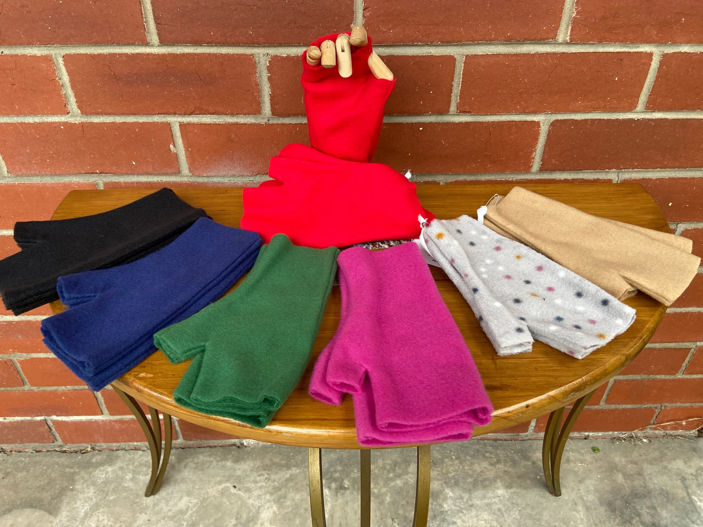 Colorful fingerless fleece gloves on a wooden table against a brick wall.