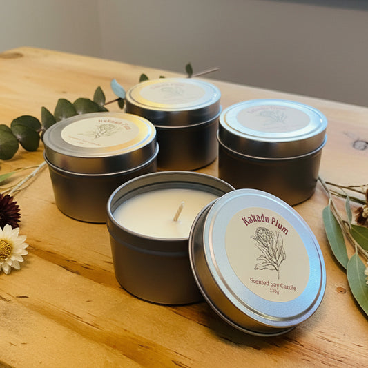 Scented soy candle in a metal tin with 'Kakadu Plum' label on a wooden surface
