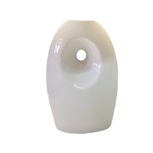 A white ceramic table lamp with a blue lampshade featuring a geometric pattern, placed on a table next to a plant.