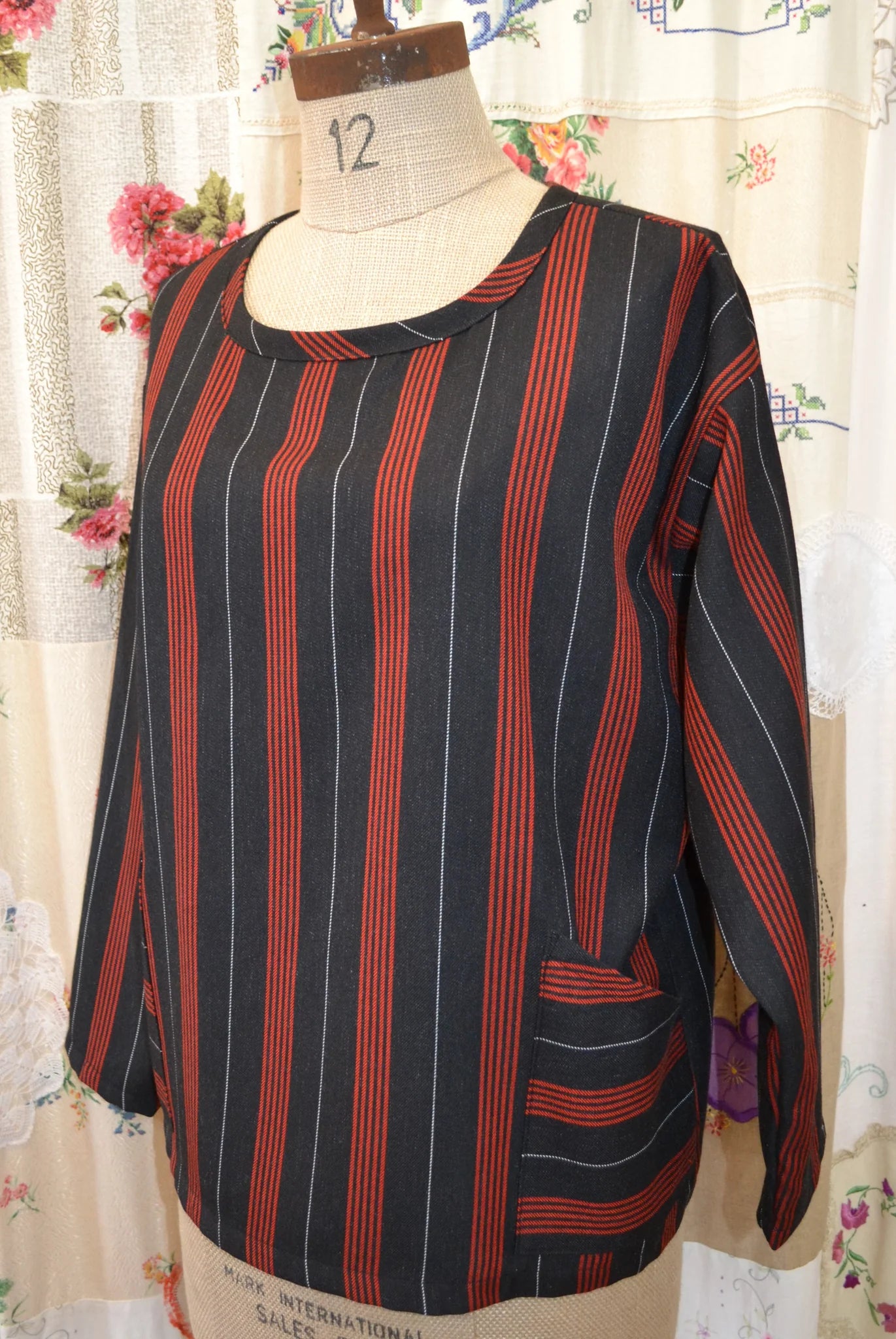Black and red striped long sleeved kite top on a mannequin against a floral curtain background