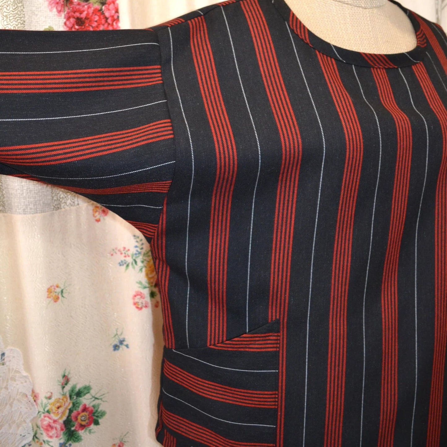 Black and red striped long sleeved kite top on a mannequin against a floral curtain background