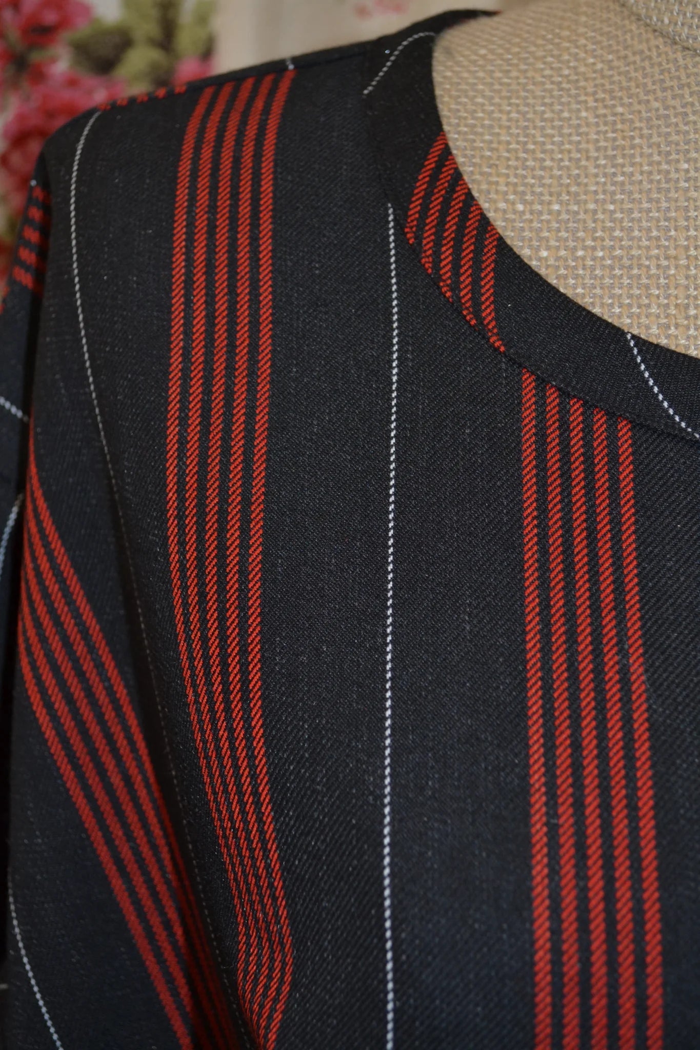 Close-up of a black fabric long sleeved kite top with red and white striped pattern on a mannequin.