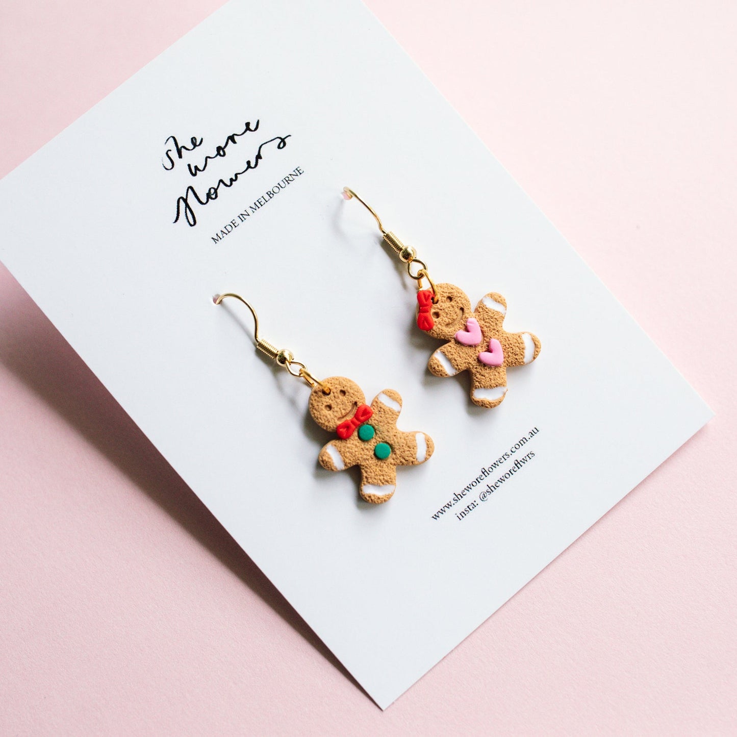 Gingerbread cookie-shaped earrings on a card with a pink background