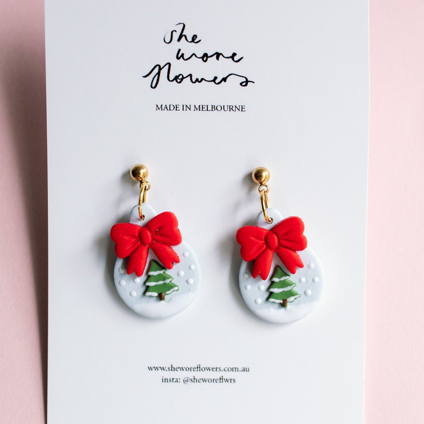 Earrings with red bows and Christmas tree designs on a white card with 'The Shone Flowers' branding.