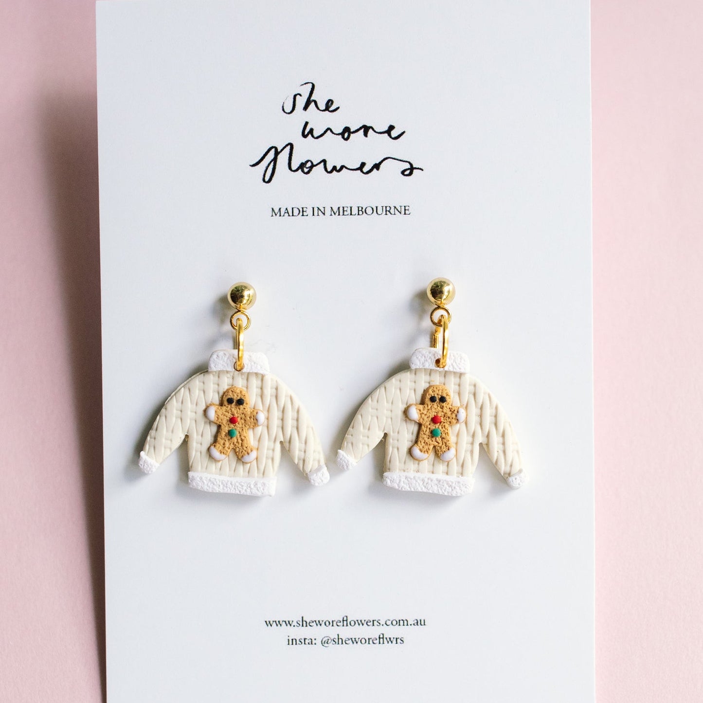 Earrings resembling knitted sweaters with teddy bears on a branded card against a pink background
