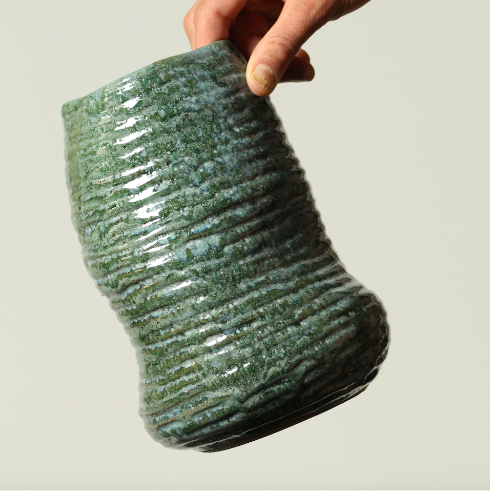 Hand holding a textured green ceramic vase against a neutral background