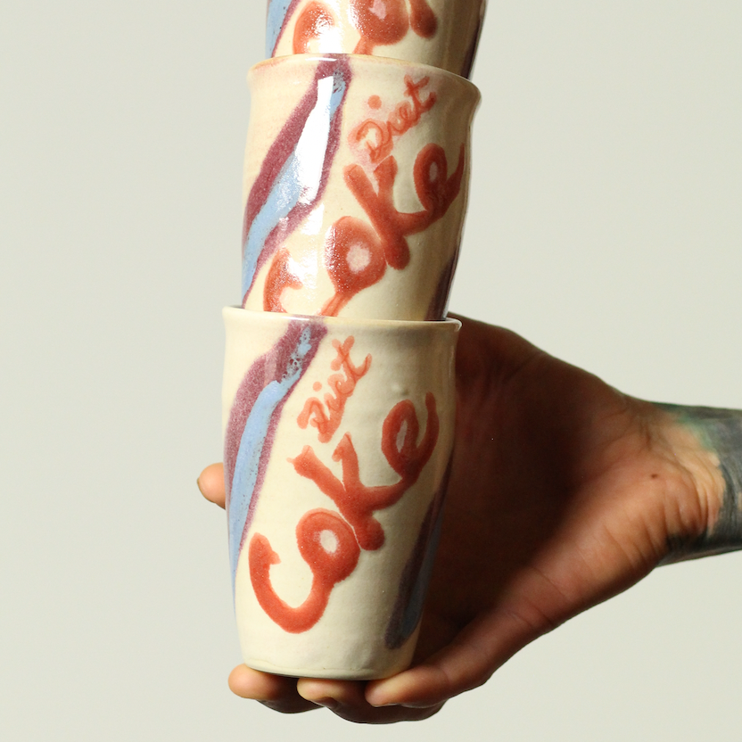 Stack of vintage-style 'Coke' cups held by a hand against a plain background
