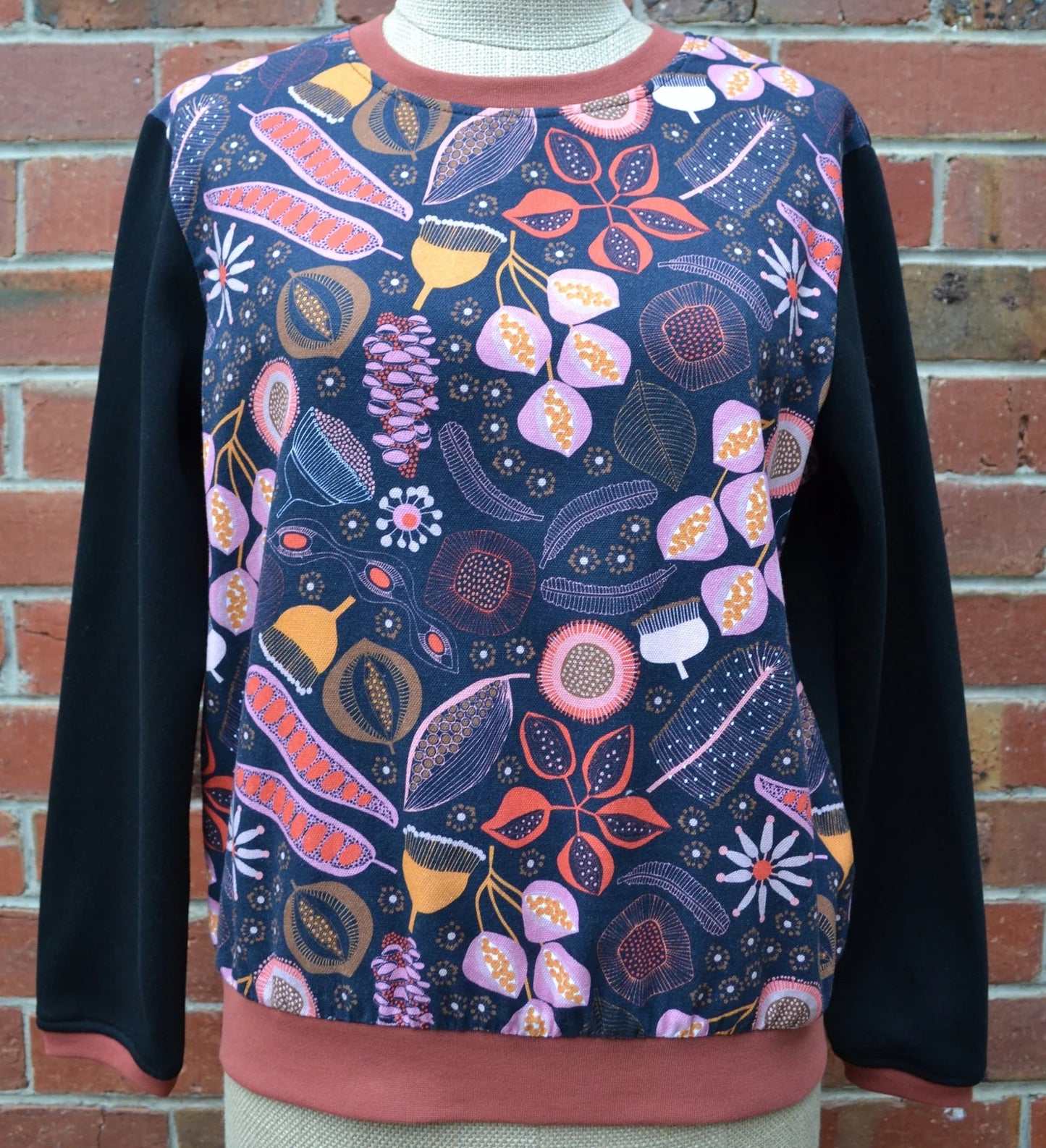 Floral patterned sweater on a mannequin against a brick wall.