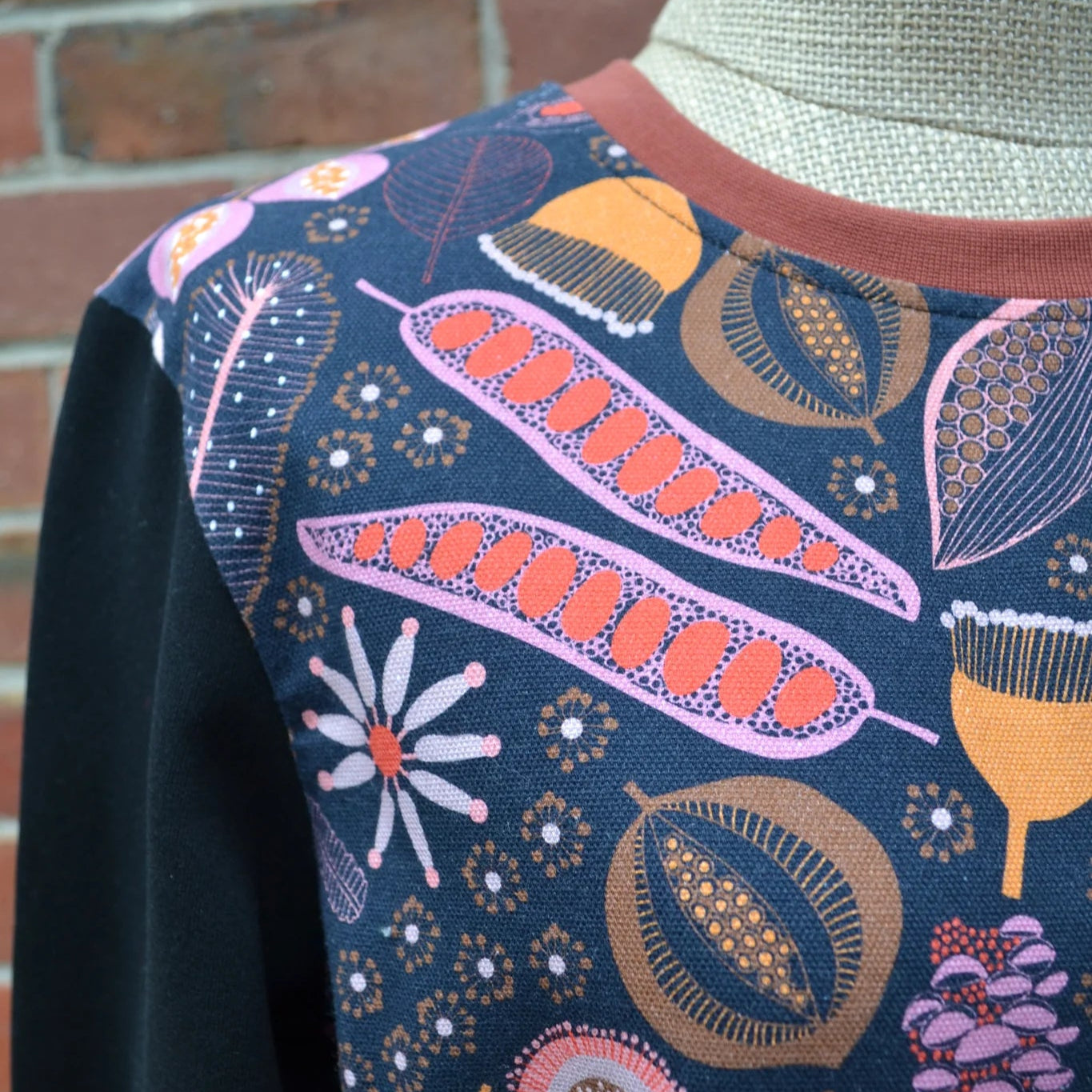 Close-up of a garment with colorful floral pattern on a mannequin against a brick wall.