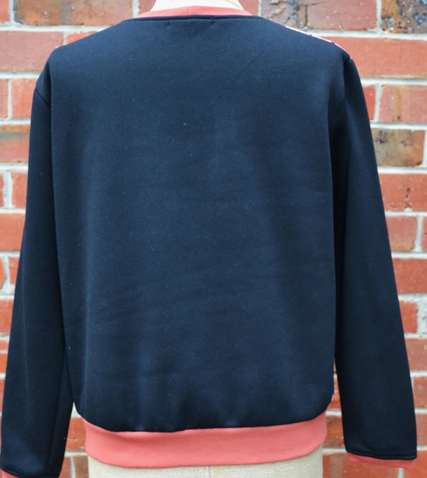 Navy blue back panel of a fleece sweater with pink trim on a mannequin against a brick wall.