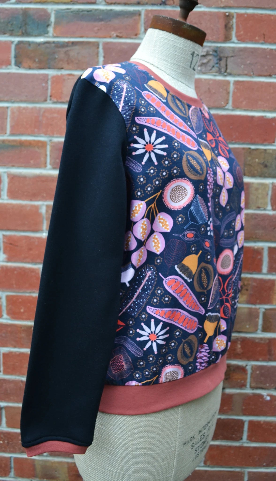 Colorful floral-patterned top on a mannequin against a brick wall.