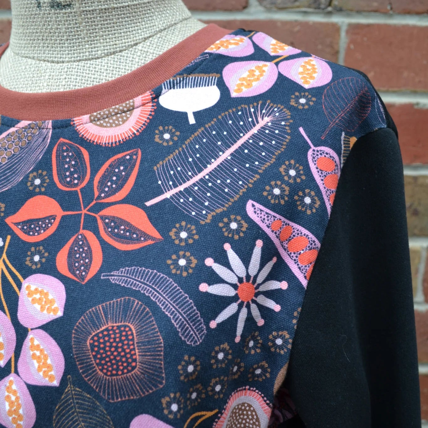 Mannequin wearing a floral-patterned garment against a brick wall.