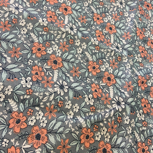 A close-up of a floral fabric pattern featuring orange, white, and light blue flowers with green leaves on a muted gray background.