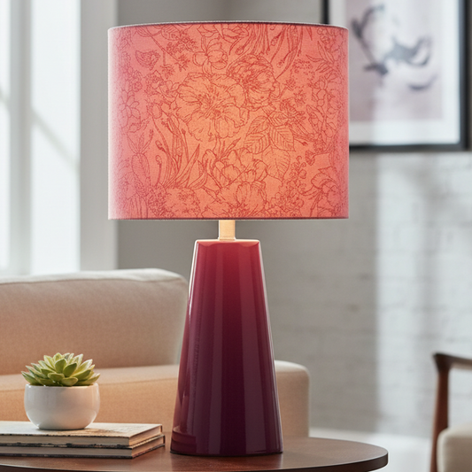 Table lamp with a pink patterned shade on a wooden table in a living room setting.