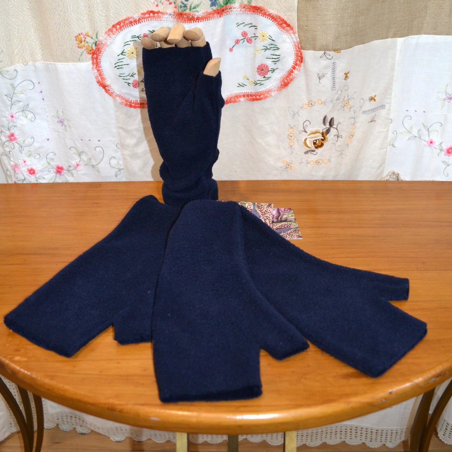 Marine blue fleece fingerless gloves on a wooden table with a floral-patterned tablecloth in the background.
