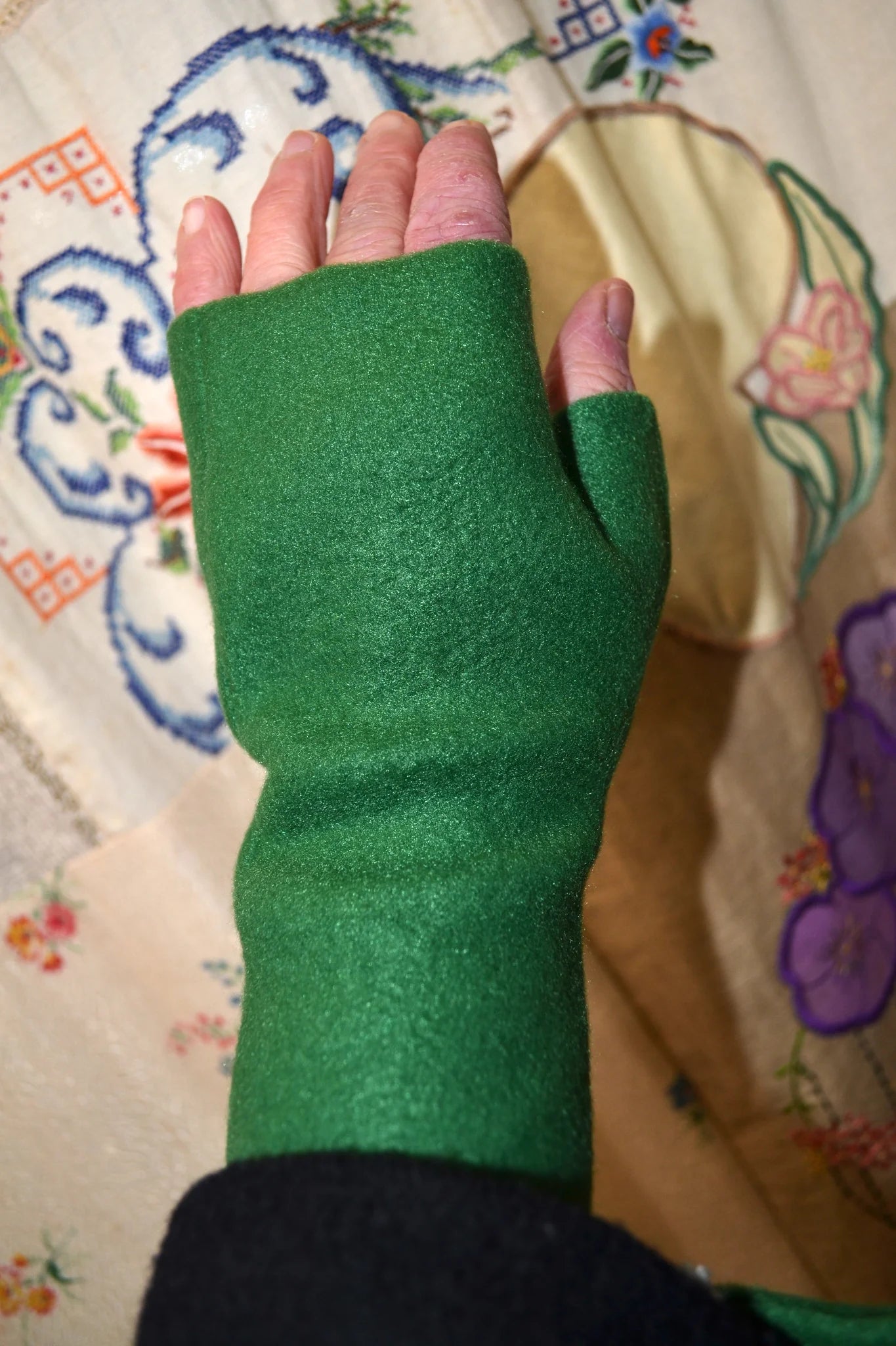 hand against a floral-patterned background wearing green fingerless gloves
