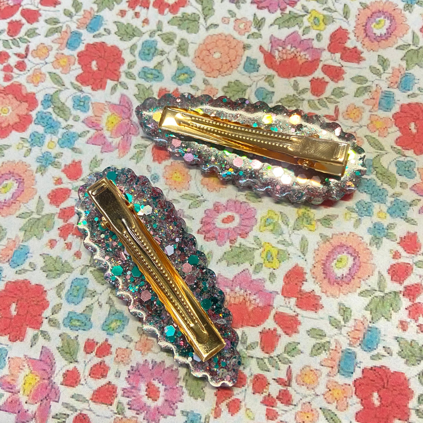 Two decorative hair clips on a floral patterned background