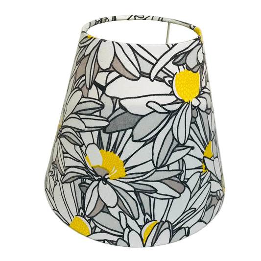 A fabric lampshade featuring a stylized daisy pattern in white, gray, black, and bright yellow, photographed against a plain off-white background.