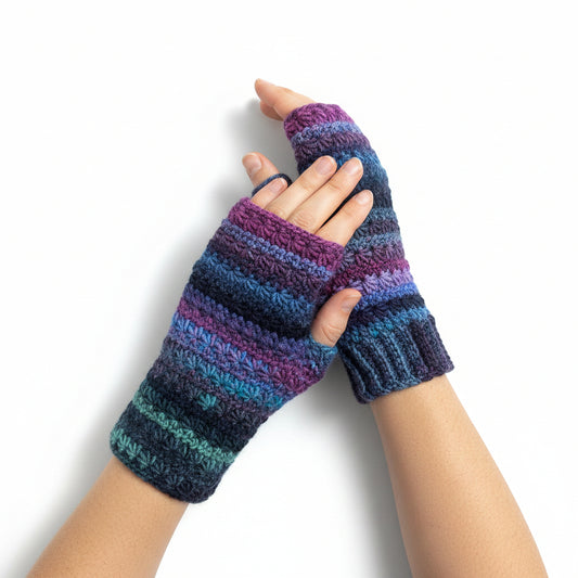 A pair of hand-crocheted fingerless gloves in a variegated yarn with stripes of purple, blue, and teal, laid flat on a light wood surface.