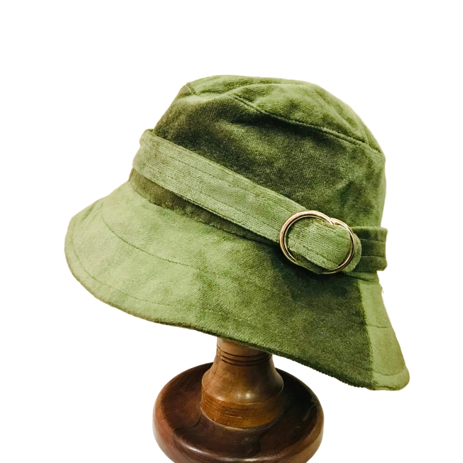 Green bucket hat with a belt and buckle on a wooden stand against a beige background