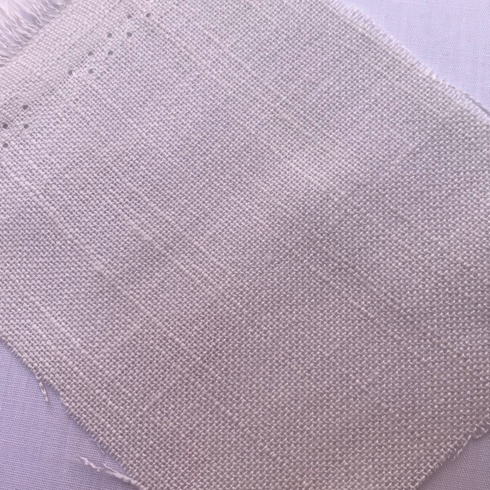 A close-up of a square fabric swatch with frayed edges, showing a light beige woven texture on a pale lavender background.