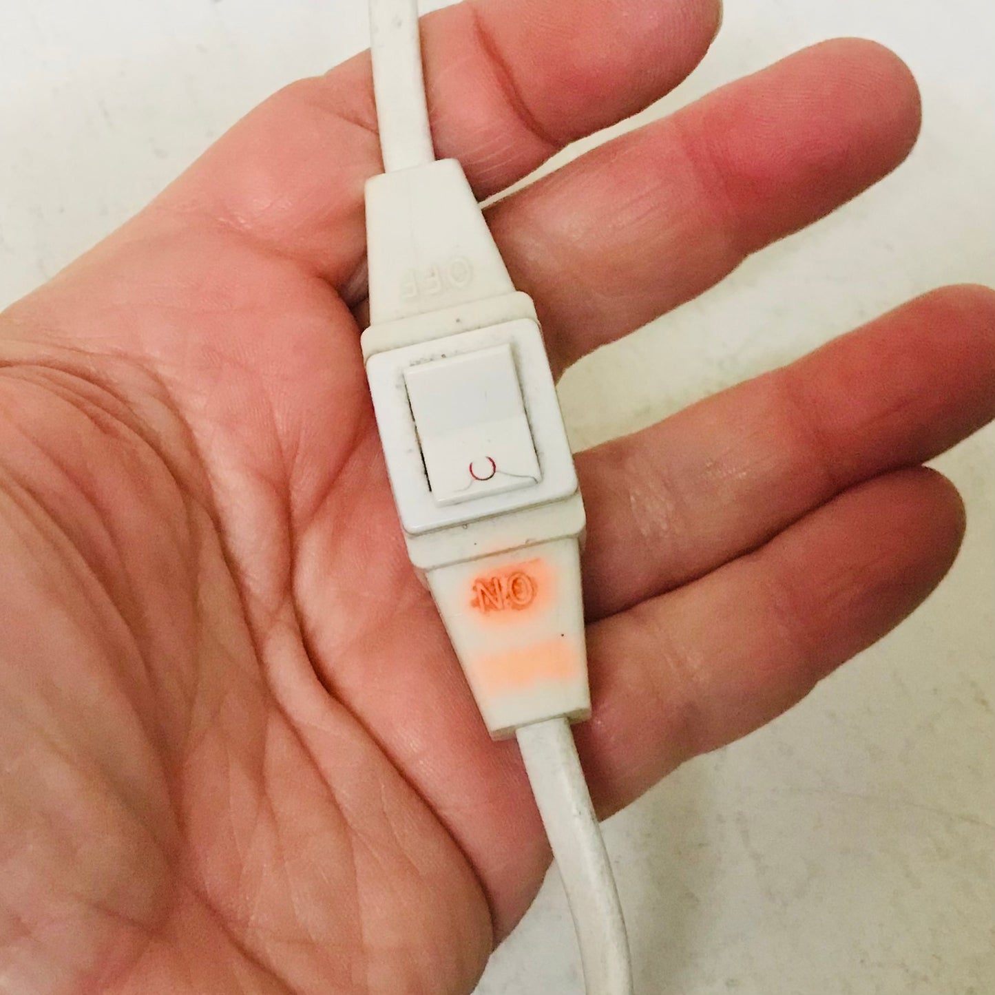 A close-up of a hand holding a white plastic electrical outlet switch connector with a small orange stain or residue near the base.