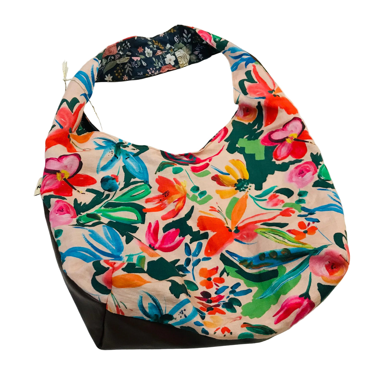 A slouchy hobo shoulder bag with a vibrant multicolor floral print on a light beige background, featuring a solid dark brown bottom panel and a dark navy patterned lining inside the strap, shown on a plain white background.