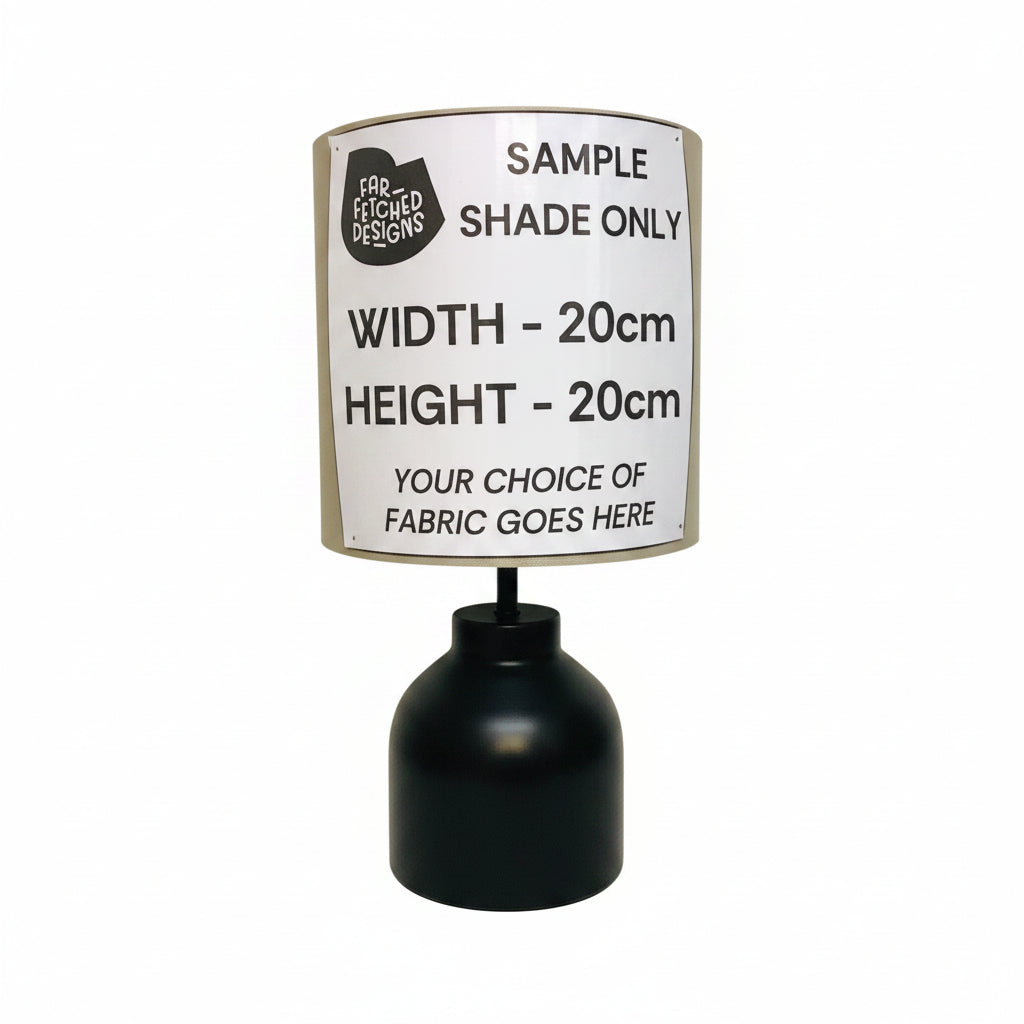 A black table lamp base with a custom fabric shade cover printed with sample sizing information, set against a plain off-white background.