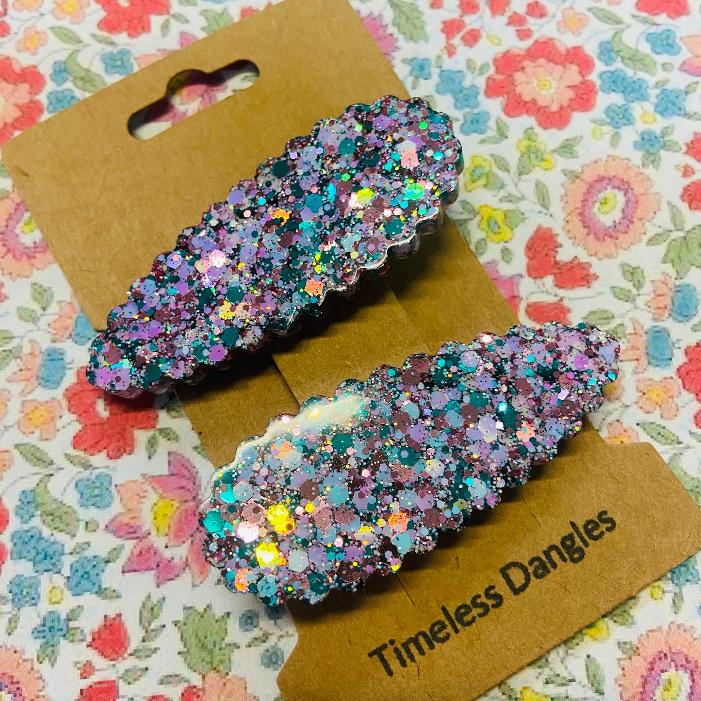 Two glittery hair clips on a 'Timeless Dangles' card with a floral background