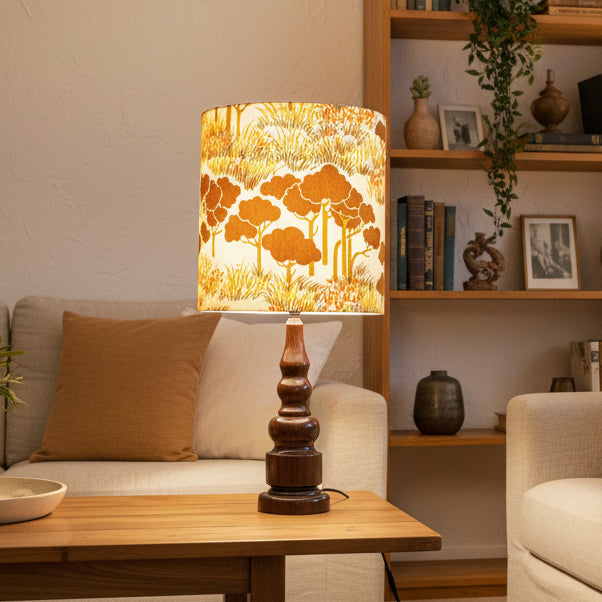 Lamp with a cylindrical shade featuring a forest design on a white wall background.