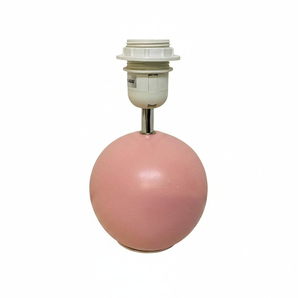 A pink spherical lamp base with a white threaded socket and metal stem, photographed against a plain off-white wall and floor.