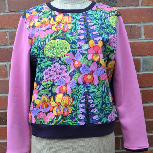 Colorful floral-patterned sweatshirt with pink sleeves against a brick wall.