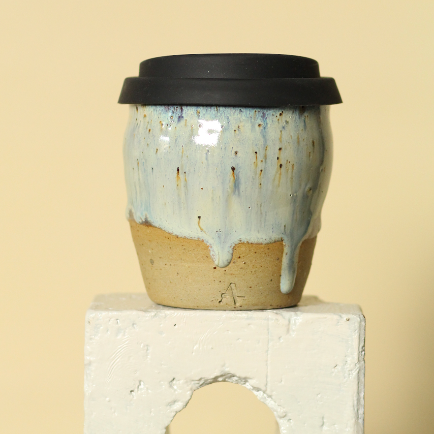 Ceramic coffee cup with a black lid on a beige background