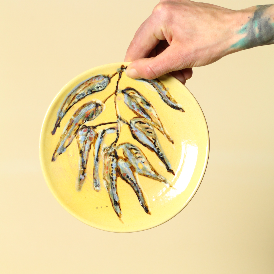 Hand holding a yellow plate with small fish on a beige background