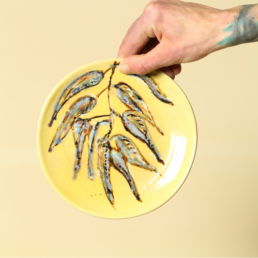 Hand holding a yellow plate with small fish on a beige background