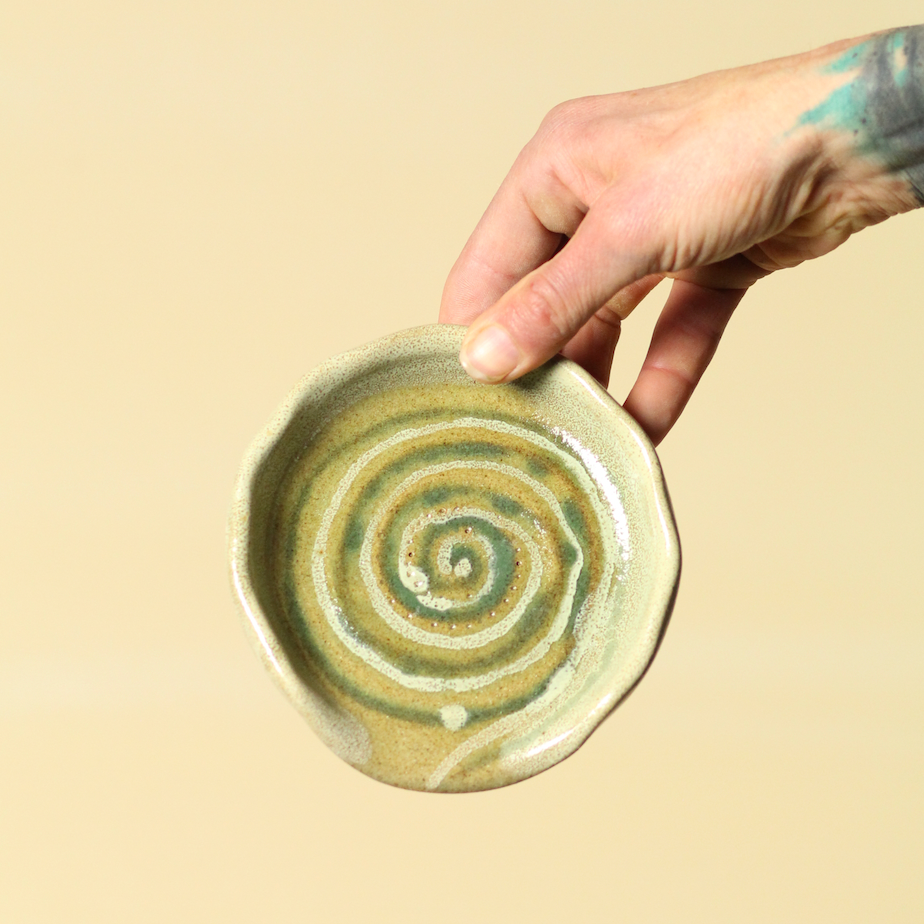 Hand holding a ceramic dish with a spiral design on a beige background