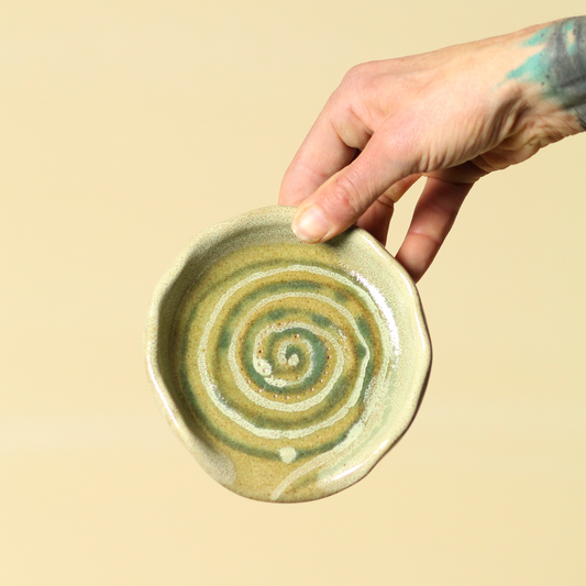 Hand holding a ceramic dish with a spiral design on a beige background
