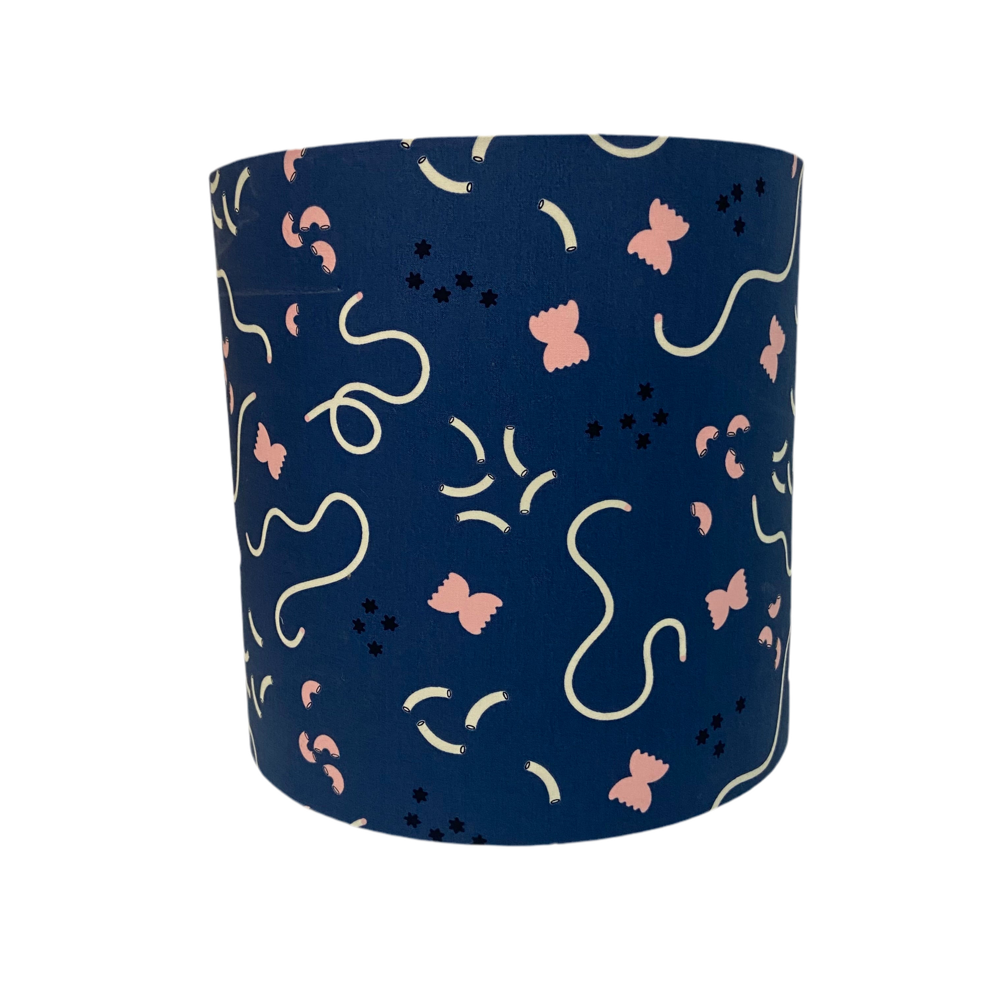 Navy blue cylindrical lampshade with pink and white abstract patterns of pasta and macaroni on a white background