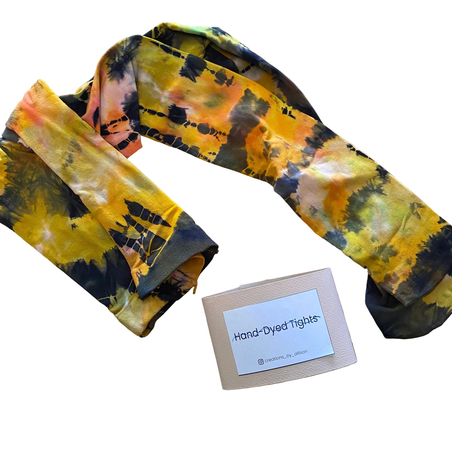 Hand-dyed tights with a tie-dye pattern on a wooden surface, accompanied by a label.