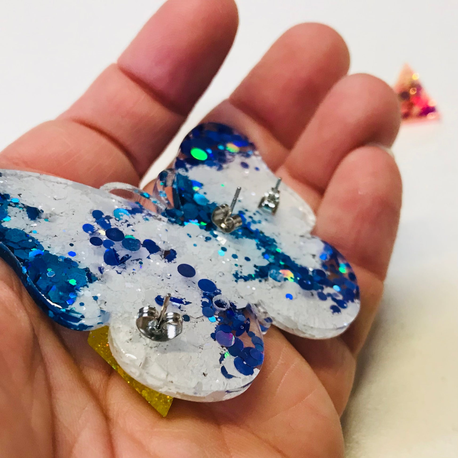 Butterfly-shaped object with blue glitter held in a hand against a white background