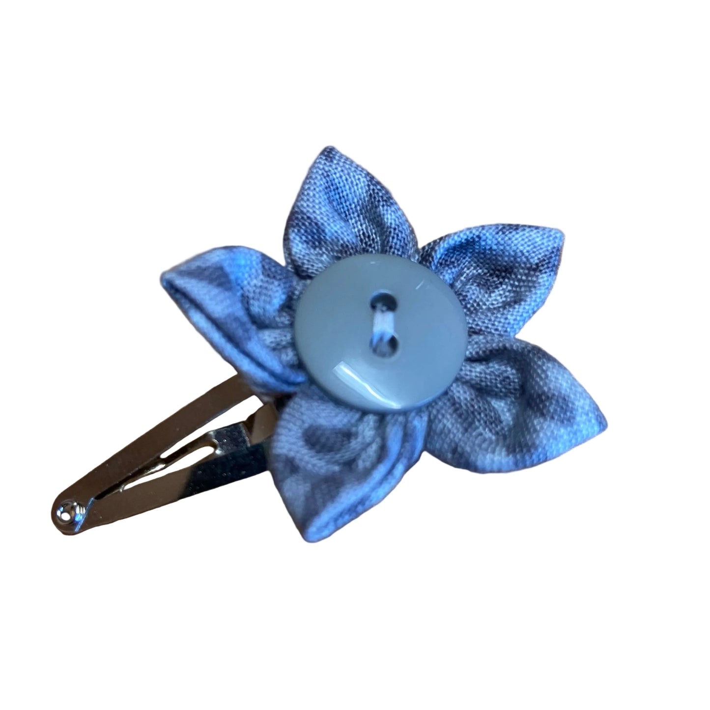 Blue flower-shaped hair clip with a button on a wooden surface