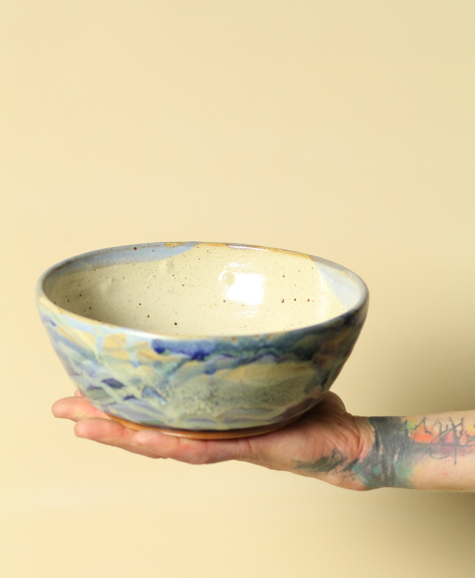 Hand holding a ceramic bowl with a watercolor design on a beige background