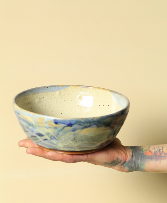 Hand holding a ceramic bowl with a watercolor design on a beige background
