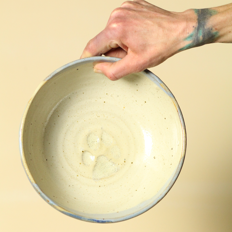 Hand holding a ceramic bowl with a speckled pattern on a beige background
